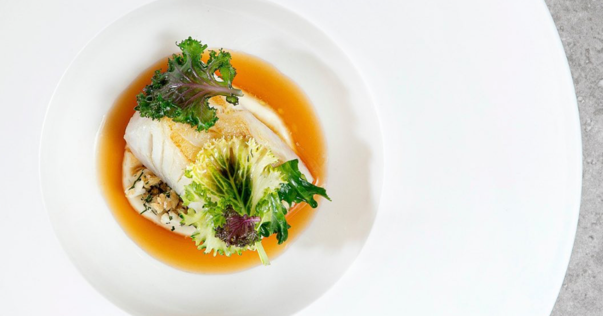 Cod dish with squid and kale on a white plate at Behind restaurant