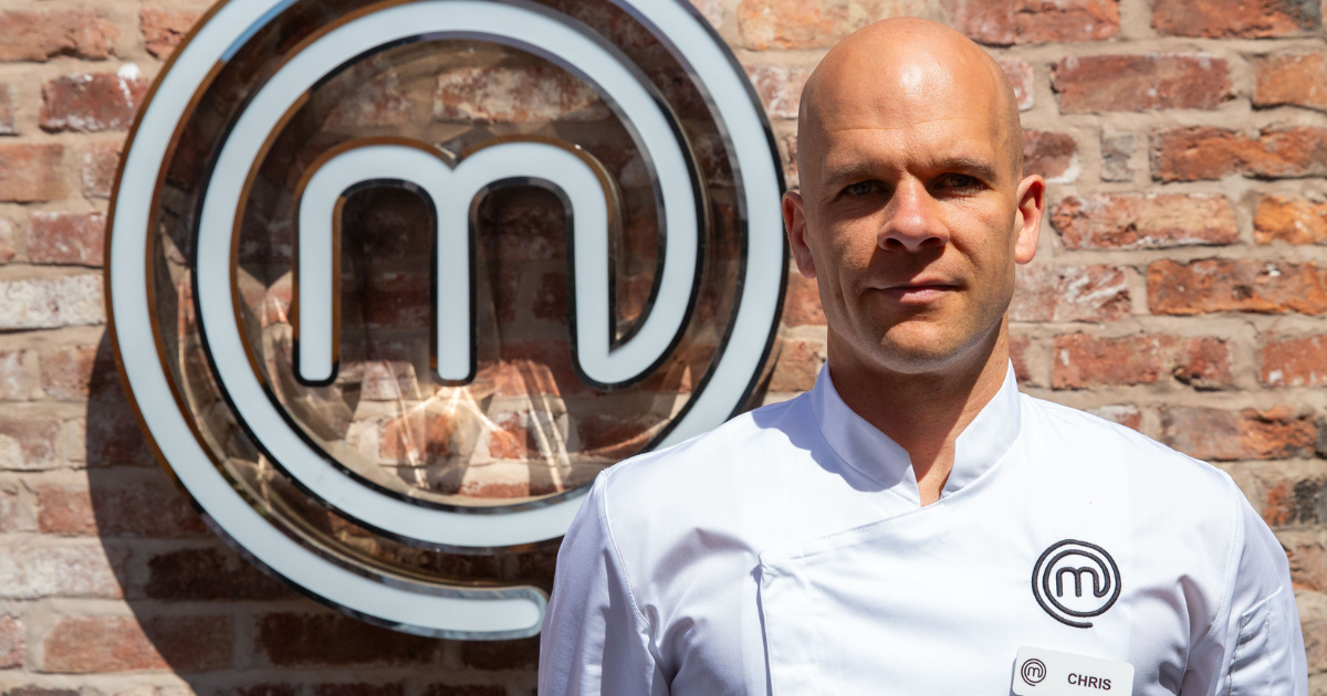 Chris Bartlett in chef whites stood in front of the MasterChef sign