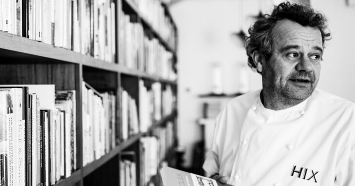 Chef Mark Hix standing beside a wall of books, wearing a HIX chef jacket